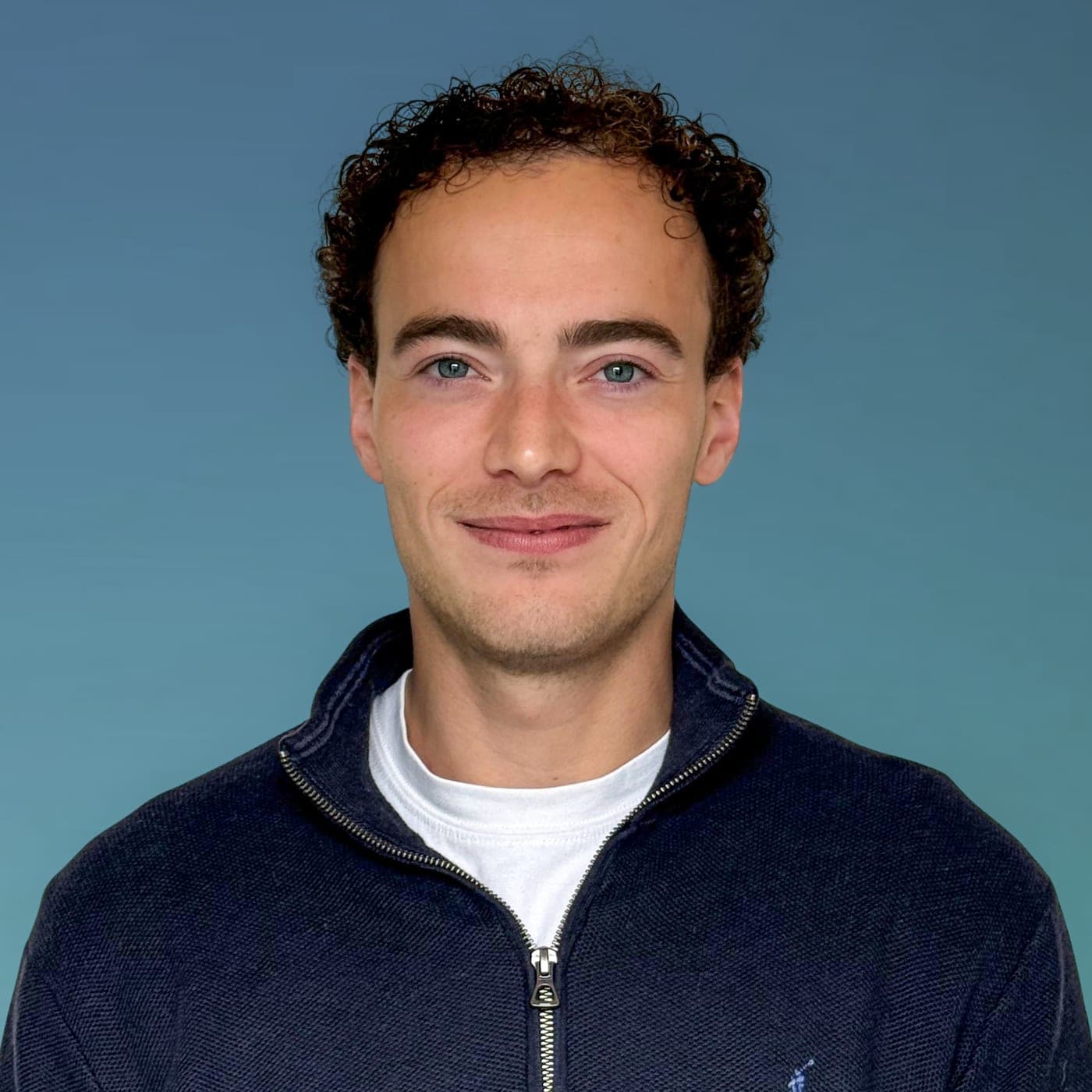 Portret van Victor Mulders, glimlachend, in een donkerblauw vest voor een blauwgroene achtergrond.